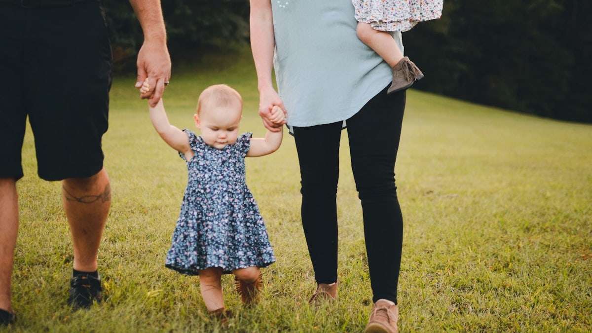 couple holding baby's arm walking on grass field
